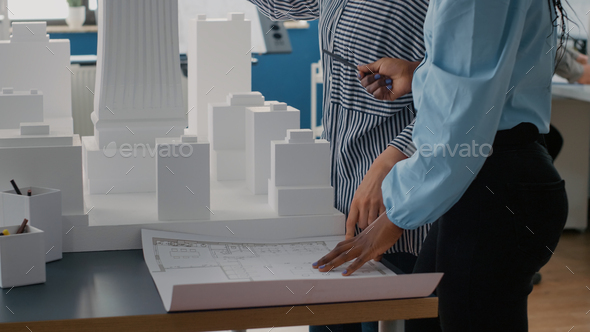 Close up of architects placing blueprints plan on table to work on urban project with building model