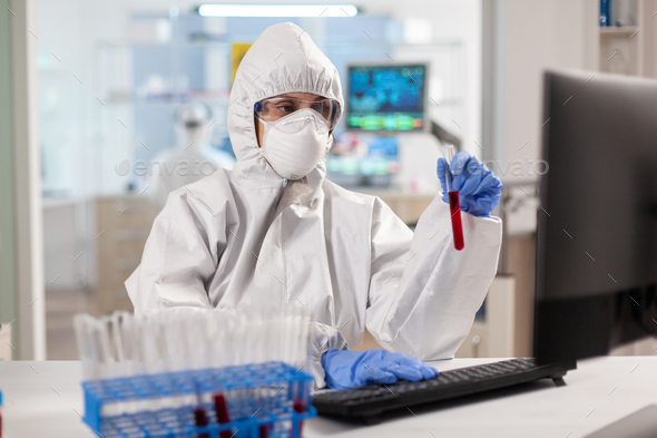 Researcher in coverall holding test tubes with blood sample for new treatment in medical laboratory