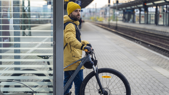 A man in winter clothes, waiting with his bike, the train.