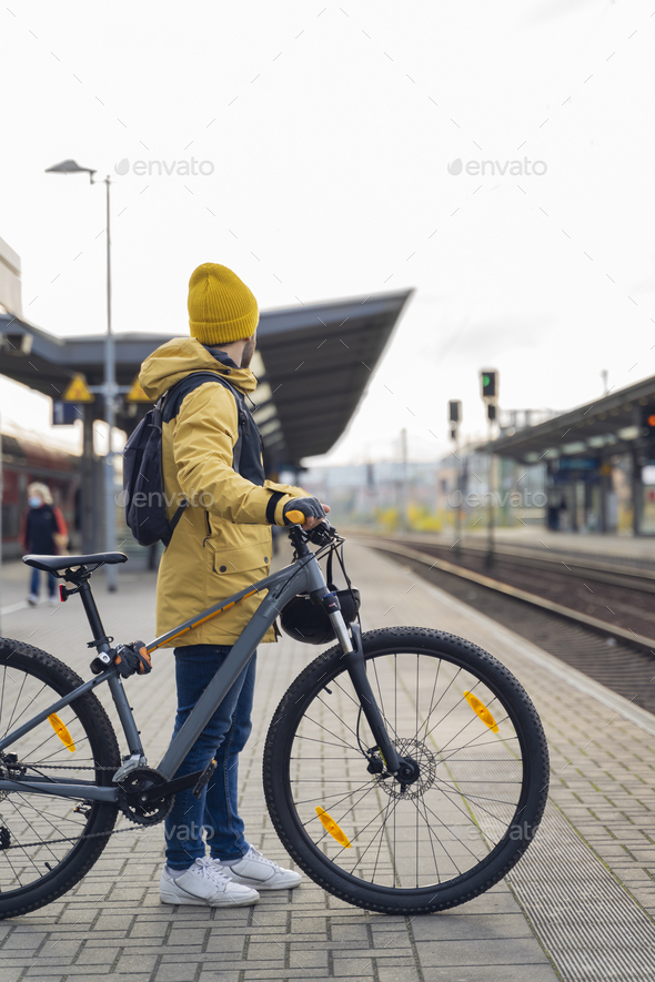 Vertical Photo of a man in winter clothes, waiting with his bike, the train.