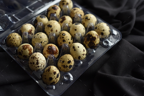 Quail eggs on a piece of black cloth. The eggs are packed in a transparent plastic container, tray
