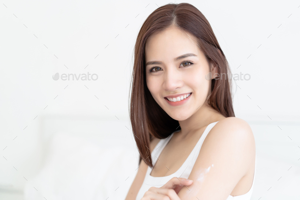 Asian woman applying body lotion on her attractive arm during her morning routine in bedroom