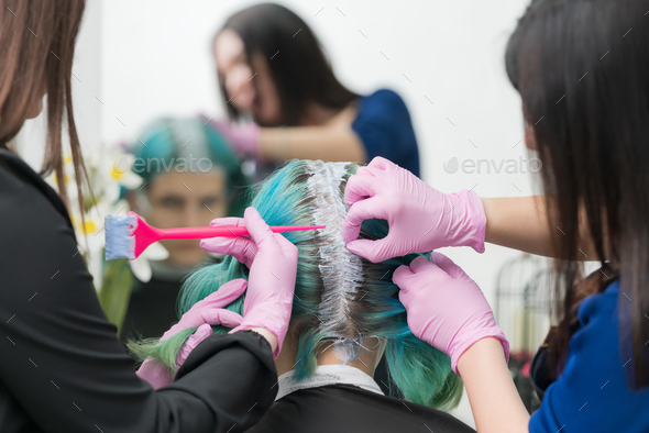 Hairdressers apply paint to hair during bleaching hair roots. Process of hair dyeing in beauty salon