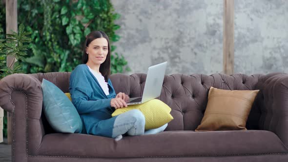 Casual Smiling Businesswoman Sitting with Crossed Legs on Couch at Home Enjoying Weekend alt