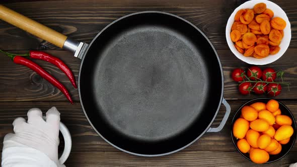 Cast iron pan on a wooden table. A chef lays out food for the frying. Kumquats, Dried Apricots etc.