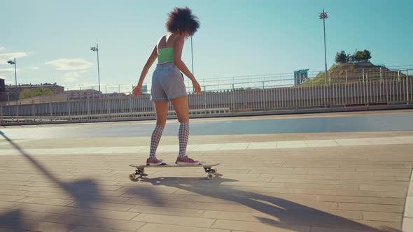Beautiful young woman cruising around the city with her longboard. alt