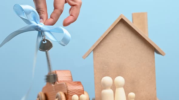 female hand holds a metal key with a blue ribbon on the background of a model house alt