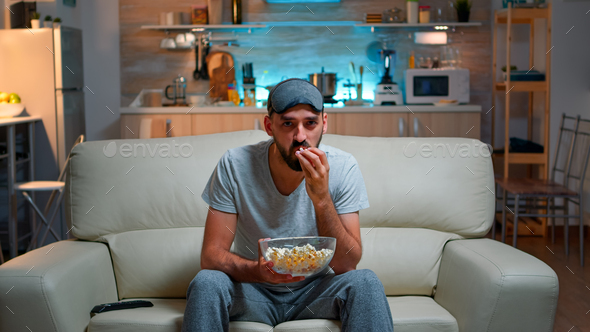 Concentrated man with sleep eye mask sitting in front of television