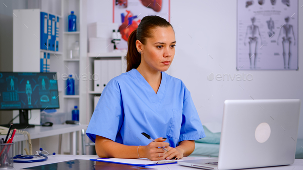 Medical assistant typing on laptop and taking notes on clipboard