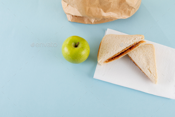 High angle view of green apple with peanut butter and jelly sandwich by paper bag on table