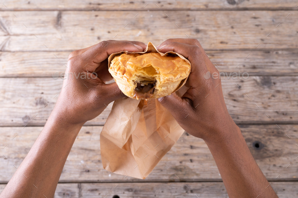 Cropped hands of african american male holding stuffed pie with missing bite over table