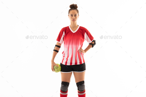 Biracial young female handball player standing with ball and hand on hip against white background