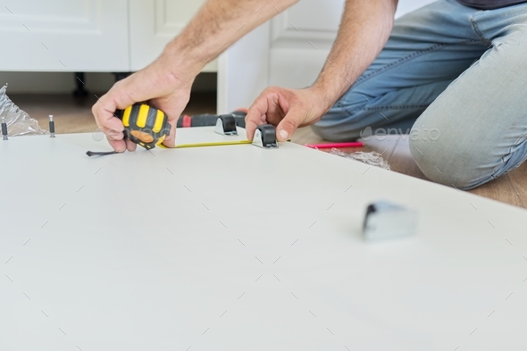 Assembling wood white furniture at home, carpenter's hands with tools and tape measure