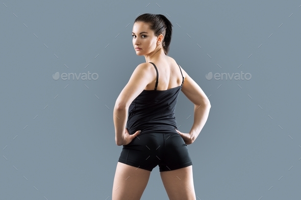 Young athletic woman in sportswear posing in studio against black