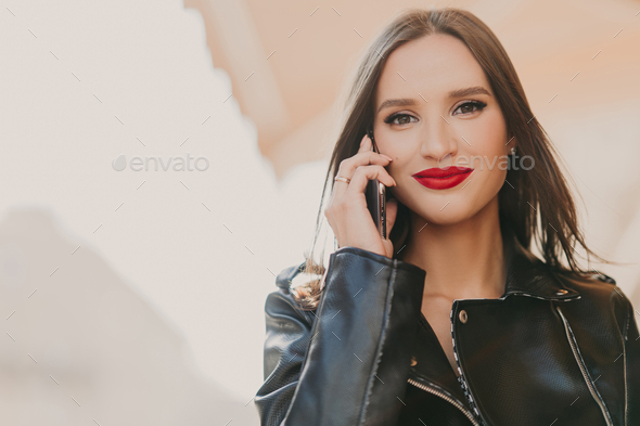 Attractive lovely female enjoys tariffs in roaming, talks on mobile phone with best friend - Stock Photo - Images