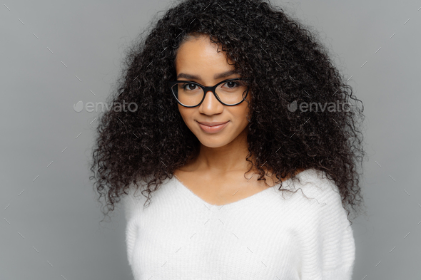 Female has satisfied expression, bushy curly hair, wears spectacles and white jumper