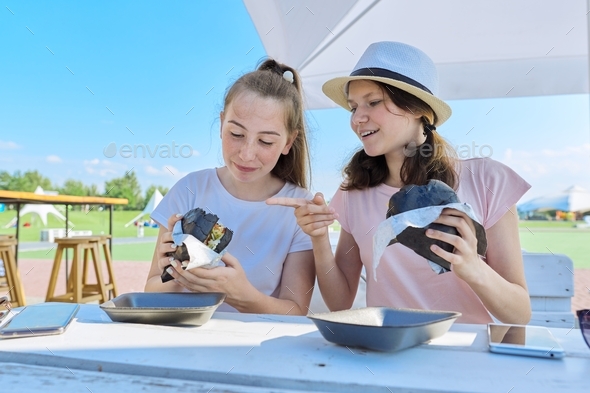 Teens two girls friends eating black burgers fast food, street food