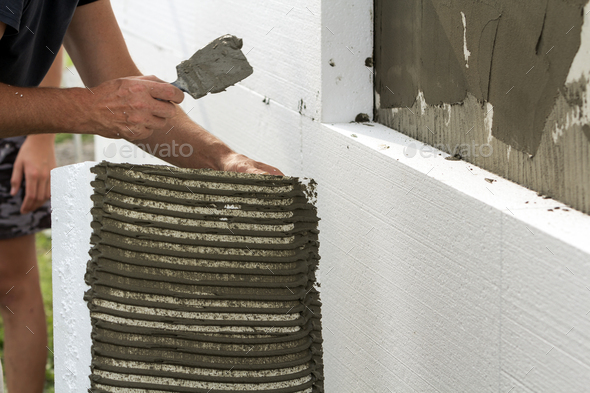 Close-up of detail of worker with trowel gluing white rigid polyurethane foam sheet to house wall