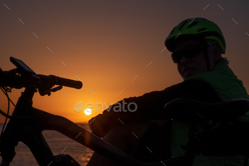 Cyclist man silhouette sitting on the beach looking at the orange beautiful sunset enjoying freedom