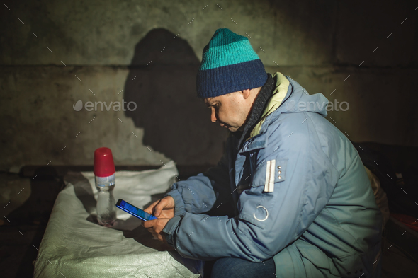 Ukrainian civil man sits in bomb shelter and reads latest braking news about the war