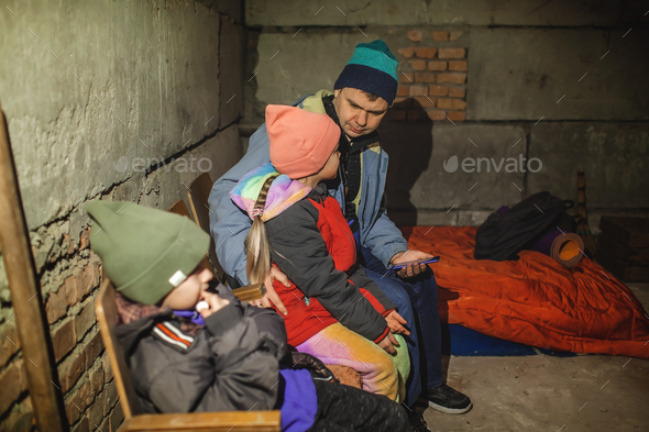 Ukrainian father with kids sits in bomb shelter and reads latest braking news about the war