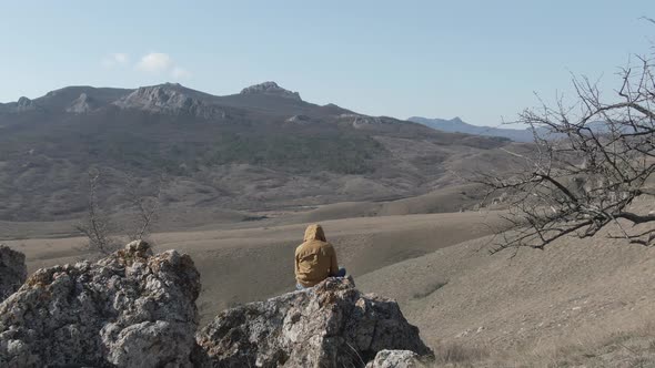 Man Sitting on a Stone on a Hillside Filming Drone