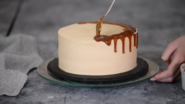 Closeup of a Pastry Chef Pouring Liquid Caramel Sauce From a Spoon on a White Cream Sponge Cake