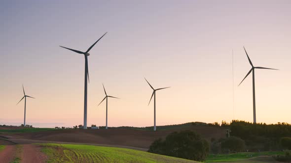 Stunning sunset silhouettes wind farm over grassy countryside, wide alt