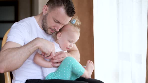 Father cuts his nails to his little daughter. Dad and baby have a great time alt
