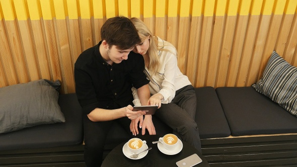 Cheerful couple sitting at coffee shop and websurfing on tablet