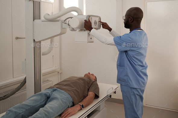 Mature patient lying on couch while doctor switching on roentgen machine