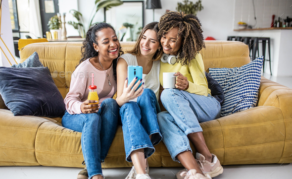 Three young multiracial women taking selfie while relaxing together at home
