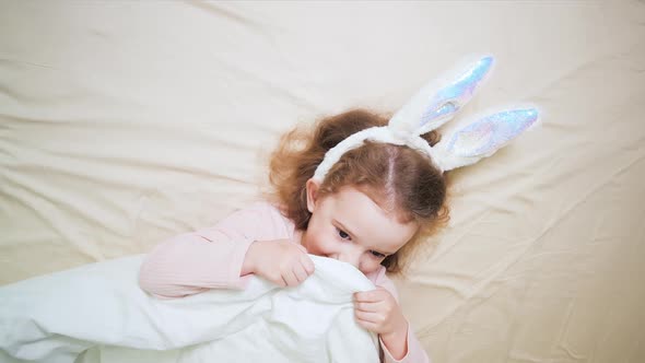 Top View a Baby Bed with a Cute Longhaired Baby Girl Under a White Blanket alt