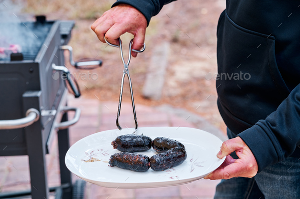 Man holding a plate with some blood sausages cooked on the barbecue