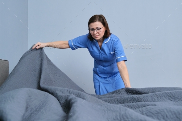 Middle aged female professional maid making bed in hotel room