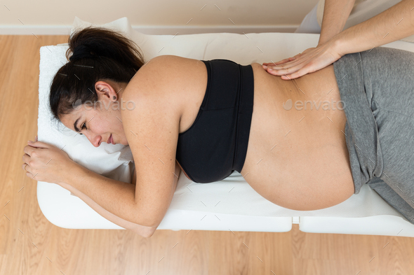 physiotherapist giving massages to the back of a pregnant woman lying on her side on a massage table