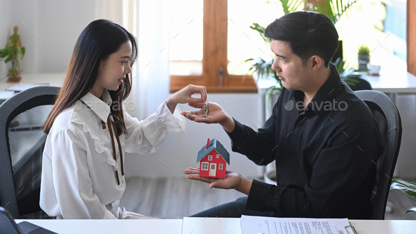 Female real estate agent giving house keys to client after signing rental lease contract.