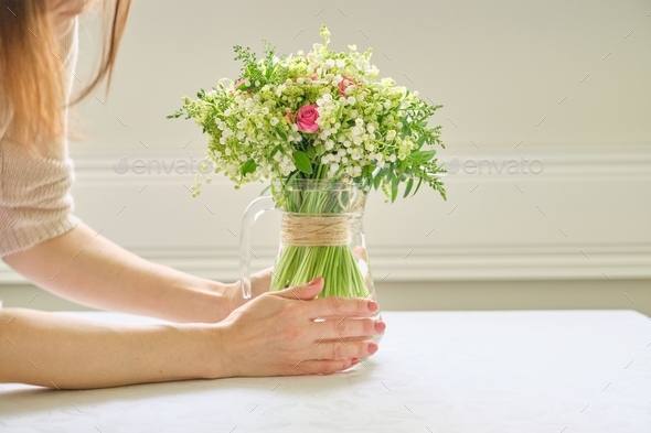 Bouquet of fresh spring flowers, woman hands holding bouquet, placing in vase on table