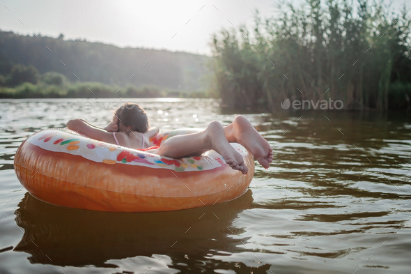 Girl relaxes on big donut inflatable ring on lake on hot summer day, happy summertime, countryside