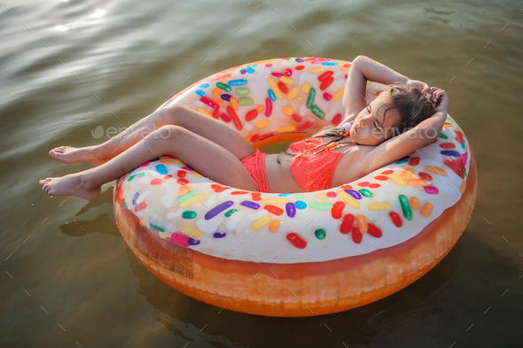 Girl relaxes on big donut inflatable ring on lake on hot summer day, happy summertime, countryside