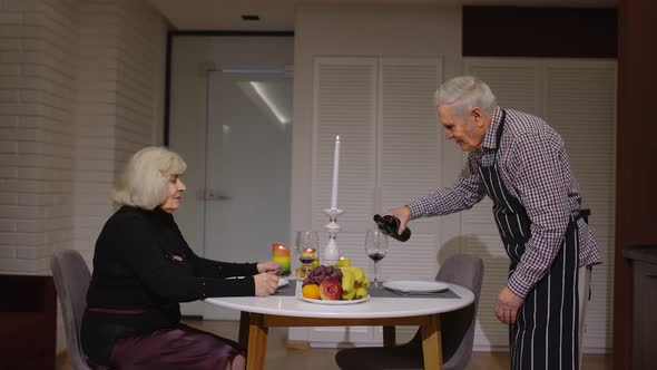 Senior Retired Couple Having Fun Drinking Wine and Eating Meal During Romantic Supper in Kitchen alt
