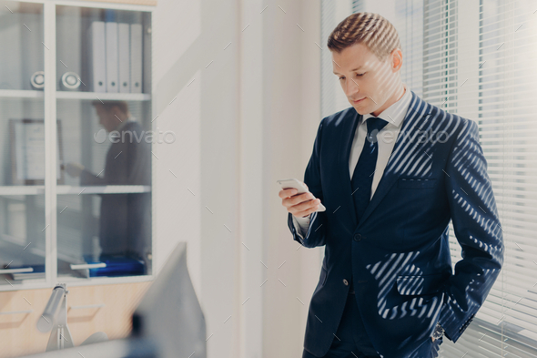 Attractive male director dressed in corporate clothing, checks email on mobile phone