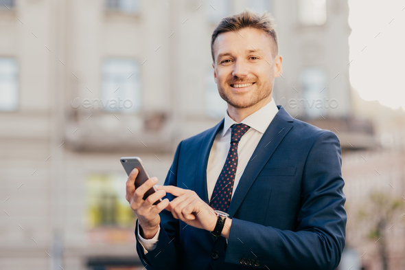 Satisfied businessman holds smart phone, reads email from investor, happy to receive good news