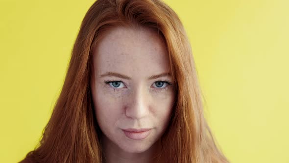 Close-up portrait of beautiful young happy red-haired woman on yellow background