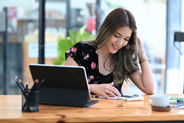 Cheerful asian woman sitting in coffee shop and using mobile phone ...