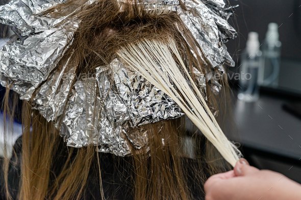 Hair stylist checking models hair during bleaching process.