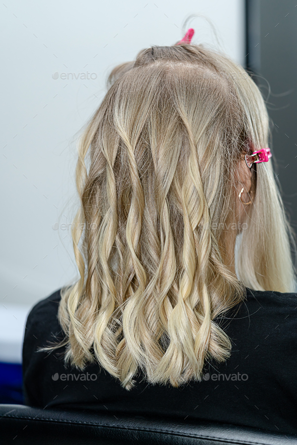 Process of hairstyling with curler for blond woman after hair bleaching.