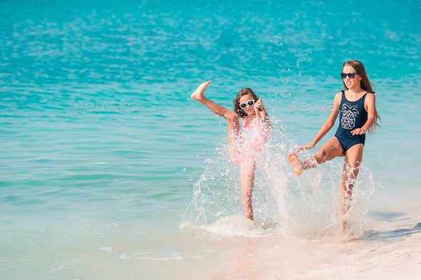 Two little happy girls have a lot of fun at tropical beach playing