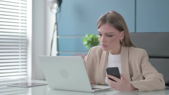 Businesswoman Using Smartphone While Using Laptop in Office alt