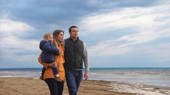 Parents with Little Daughter Walking By the Sea on Cold Day alt